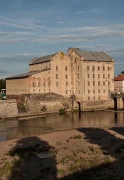 Posádkový pšeničný vodní mlýn. Pohled přes řeku na budovu mlýny a výpusť od vodního kola.