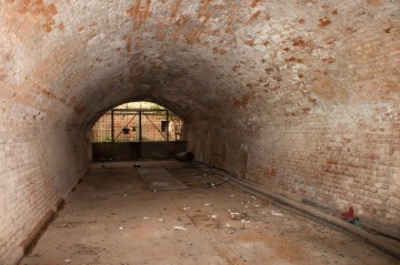 Pohled z tunelu hlavní galerie směrem do příkopu retranchementu 4. Po pravé straně fotografie zazděný vstup do prachárny. Za mříží lze spatřit otvor střílny.